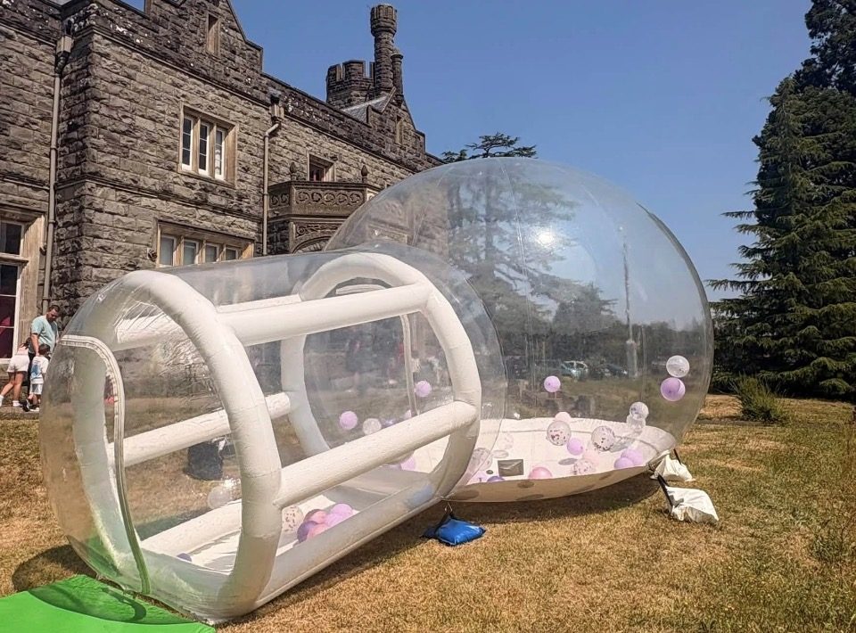 White bubble house with pink and lilac balloons set up on the lawn of a historic venue