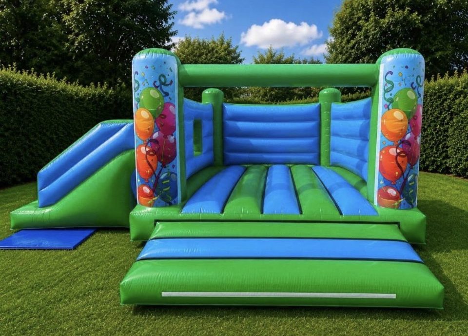 Green and blue bouncy castle with side slide and party balloon artwork