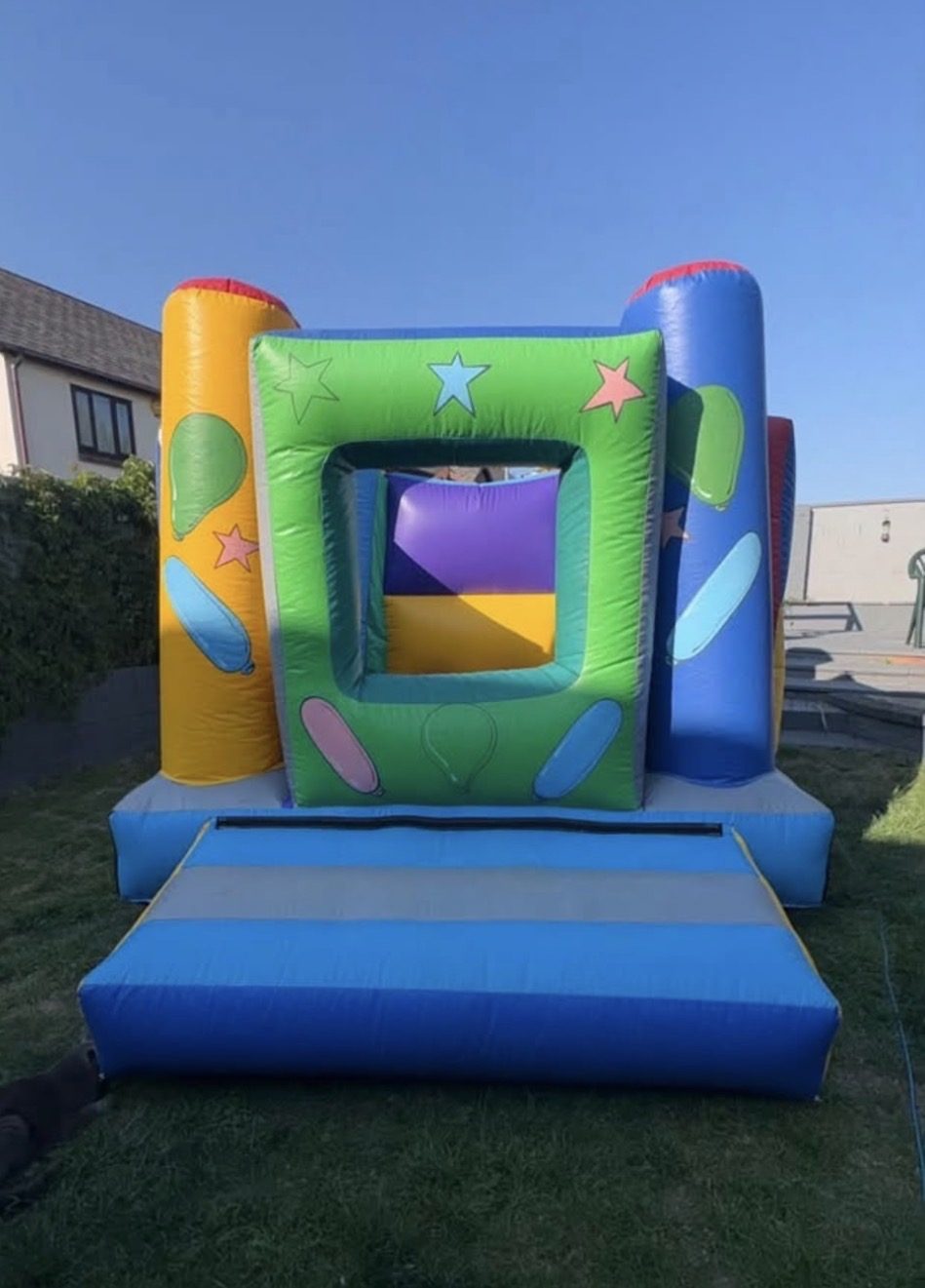 Small blue, green and yellow bouncy castle with balloon and star artwork in a garden