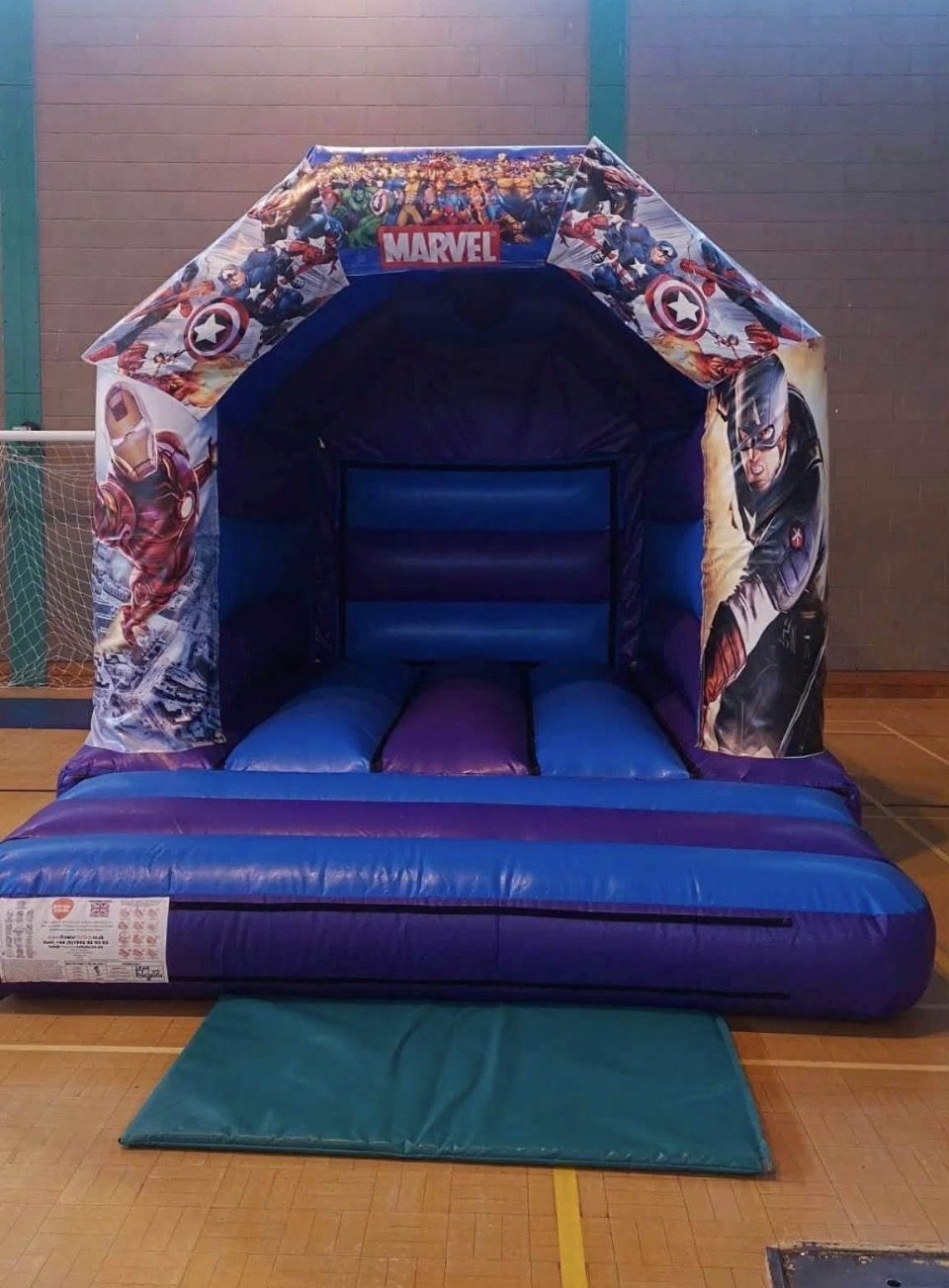 Blue and purple Marvel themed bouncy castle set up in a sports hall
