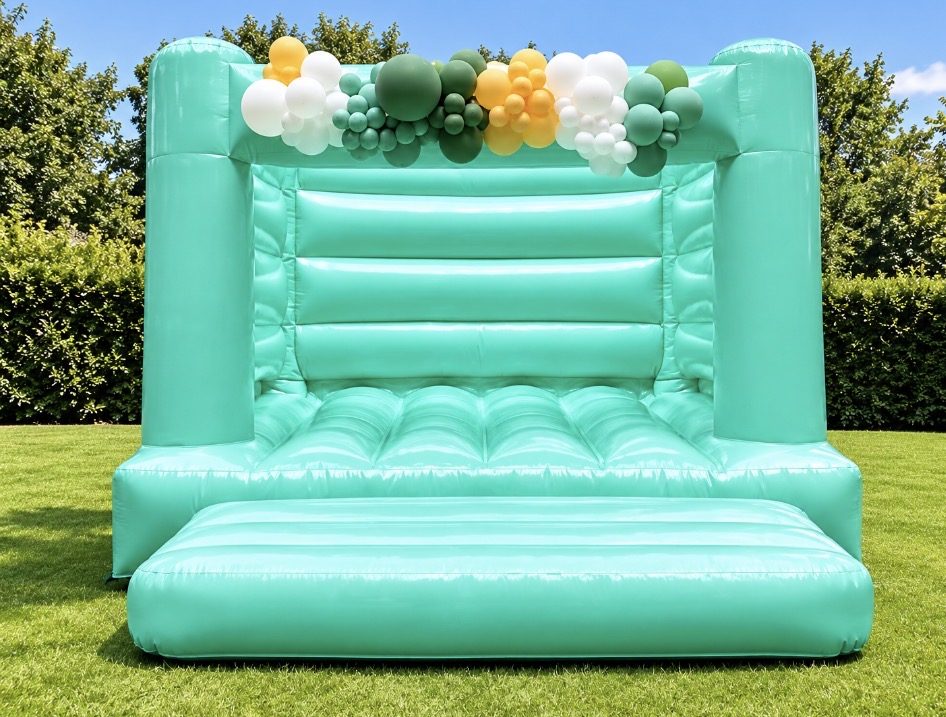 Mint green pastel bouncy castle with a green, white and gold balloon garland