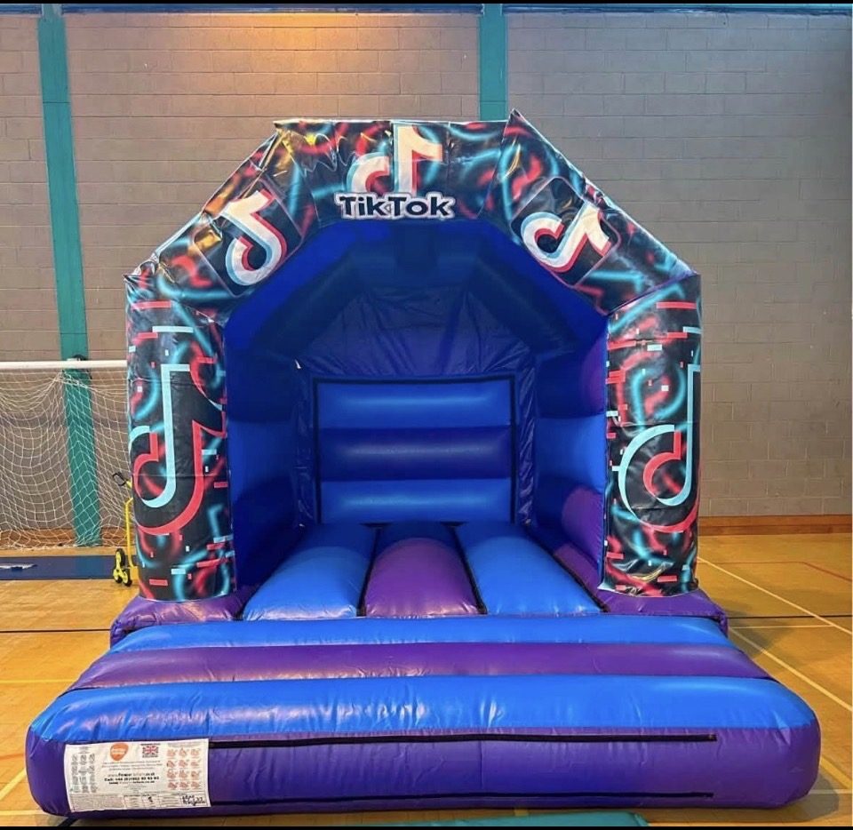 Blue and purple bouncy castle with neon TikTok artwork, set up in a sports hall