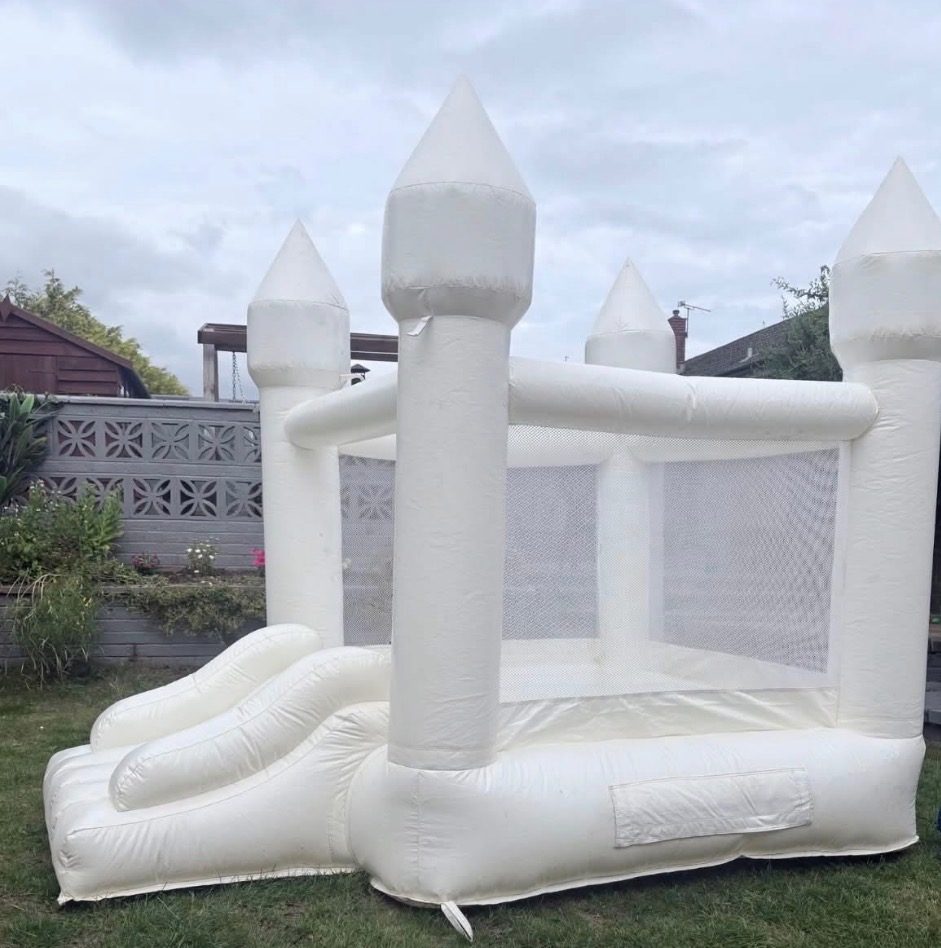 All-white bouncy castle with turrets and a small slide, set up in a back garden