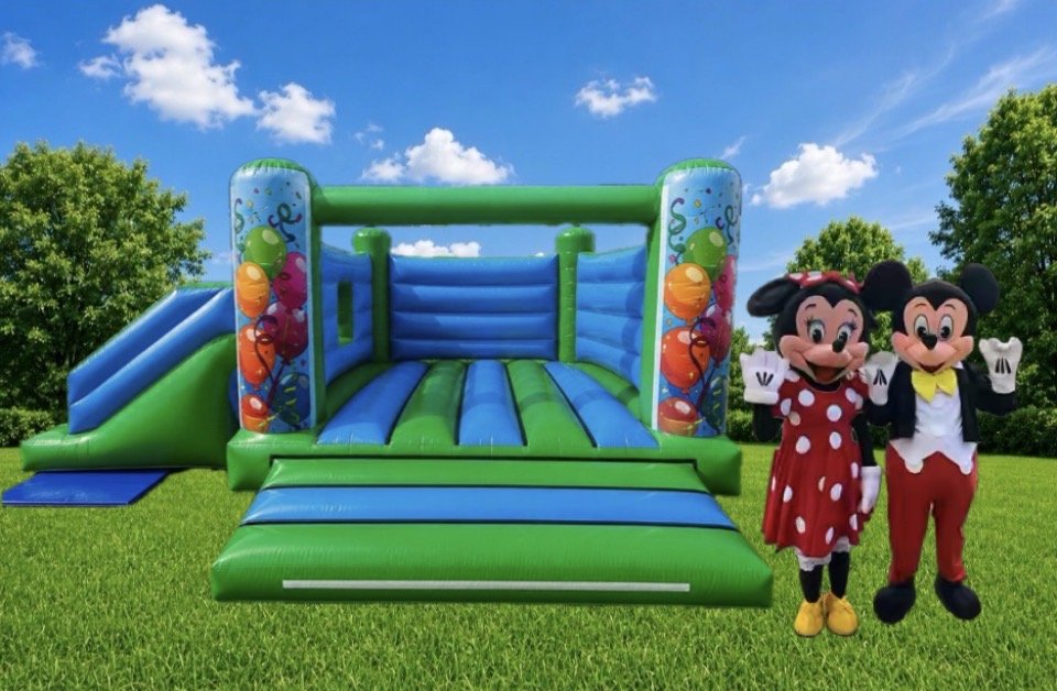 Green and blue balloon bouncy castle with slide, next to Mickey and Minnie lookalike mascots waving