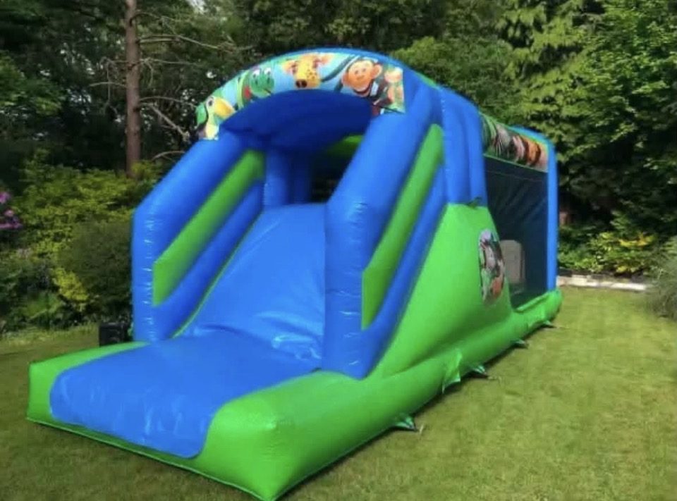 Blue and green jungle themed inflatable with a slide, set up in a garden