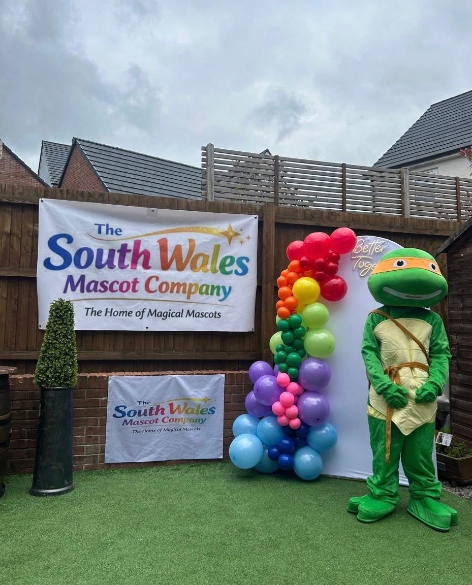 Orange-masked ninja turtle lookalike mascot beside a rainbow balloon garland