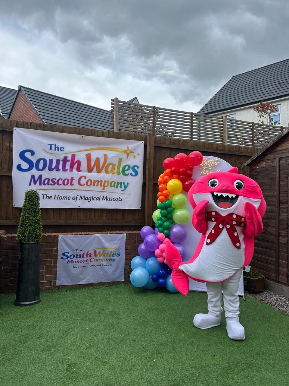 Pink shark lookalike mascot with a red polka-dot bow