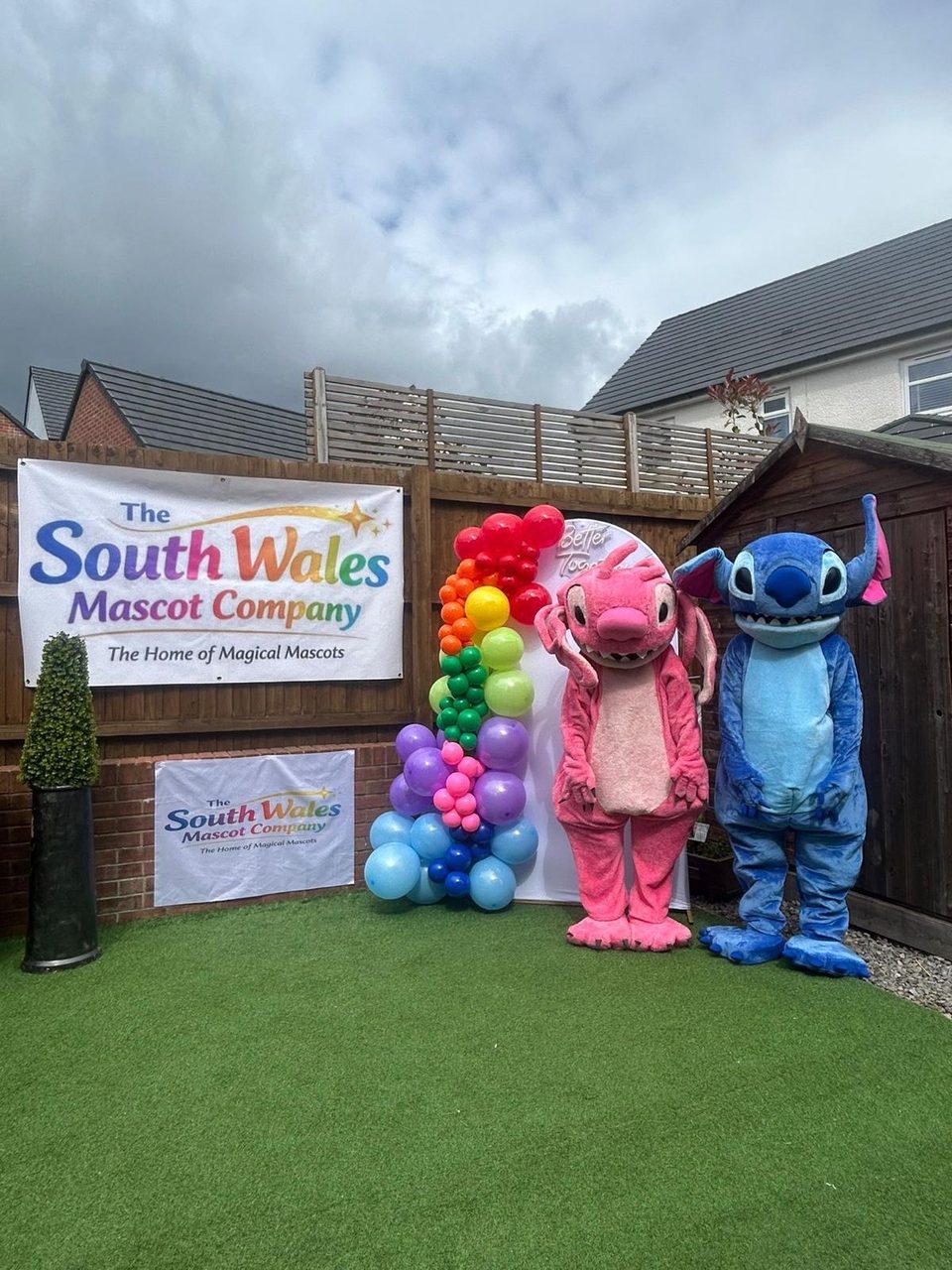 Stitch and Angel lookalike mascots standing by a rainbow balloon garland