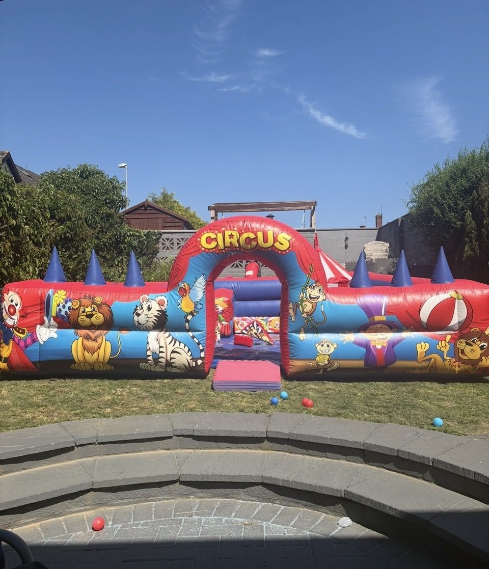 Red and blue circus themed inflatable soft play pen with an arch entrance, set up in a garden